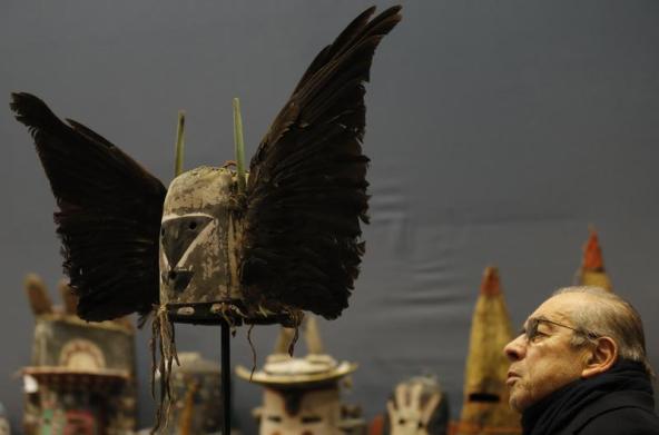 (A man looks at an antique tribal mask, Tumas Crow Mother, circa 1860-1870, revered as a sacred ritual artifact by the Native American Hopi tribe in Arizona, displayed at the Drouot auction house ahead of its sale in Paris December 9, 2013. REUTERS/Christian Hartmann)